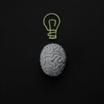 A gray brain sculpture with a light bulb drawn above it on a black background.